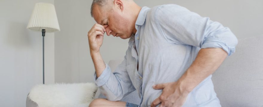 middle-aged white male sitting on couch with hand on stomach, clearly distraught and in pain