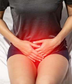 woman sitting down with pain in the vaginal area, highlighted in red